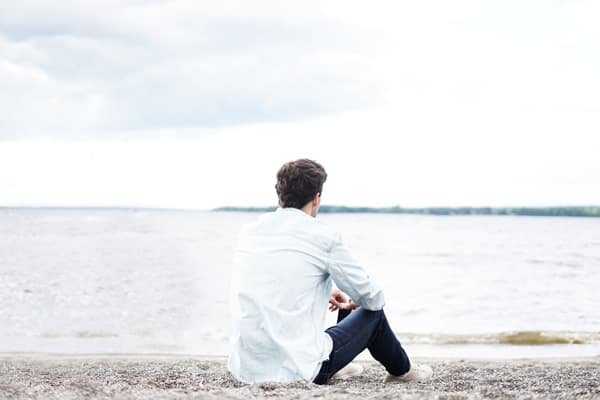 A man sitting on the beach looking out at water.