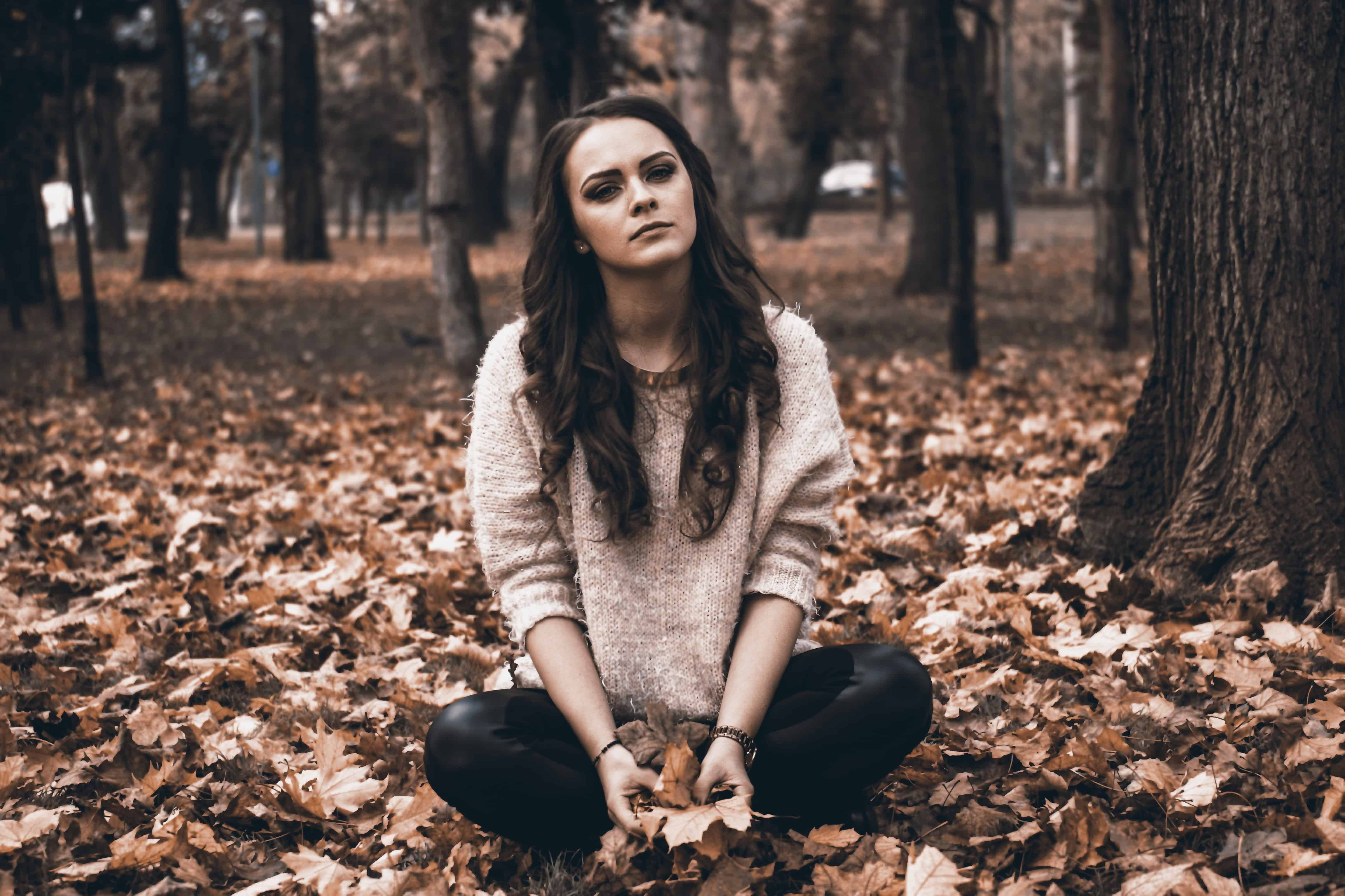 A woman sitting on the ground in leaves.
