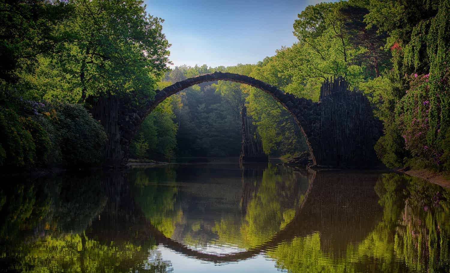 arch bridge over clear lake with reflection