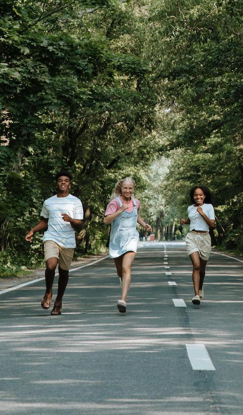 teenagers running along tree lined road smiling