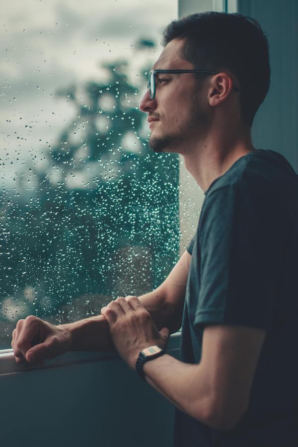 man looking out of rainy window